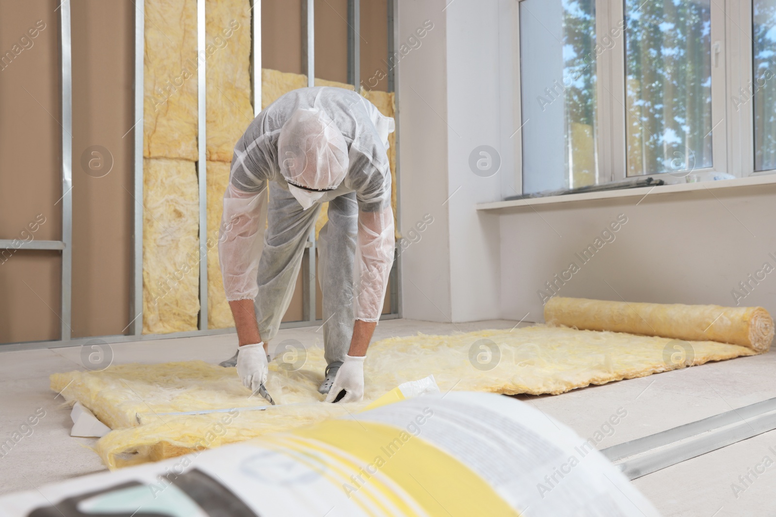 Photo of Worker measuring and cutting insulation material indoors