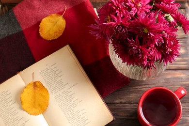 Photo of Beautiful chrysanthemum flowers, cup of tea and book on wooden table indoors, flat lay
