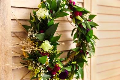 Photo of Beautiful wreath made of flowers and leaves hanging on wooden folding screen, closeup