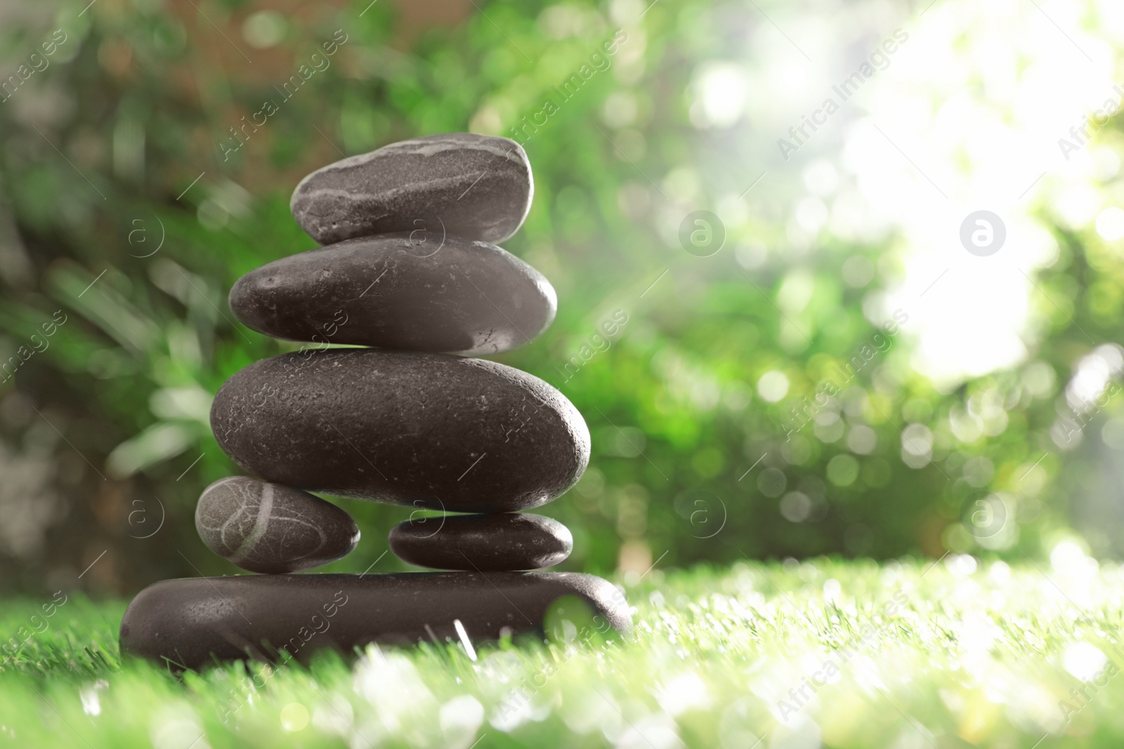 Photo of Stack of stones on green grass against blurred background, space for text. Zen concept