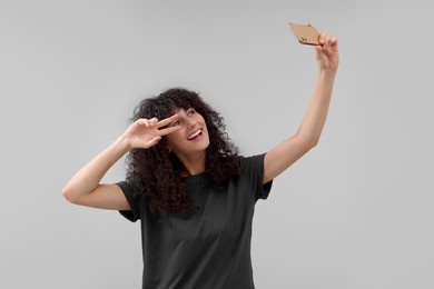 Beautiful young woman taking selfie on light grey background