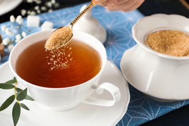 Photo of Woman putting brown sugar into tea cup at table, closeup