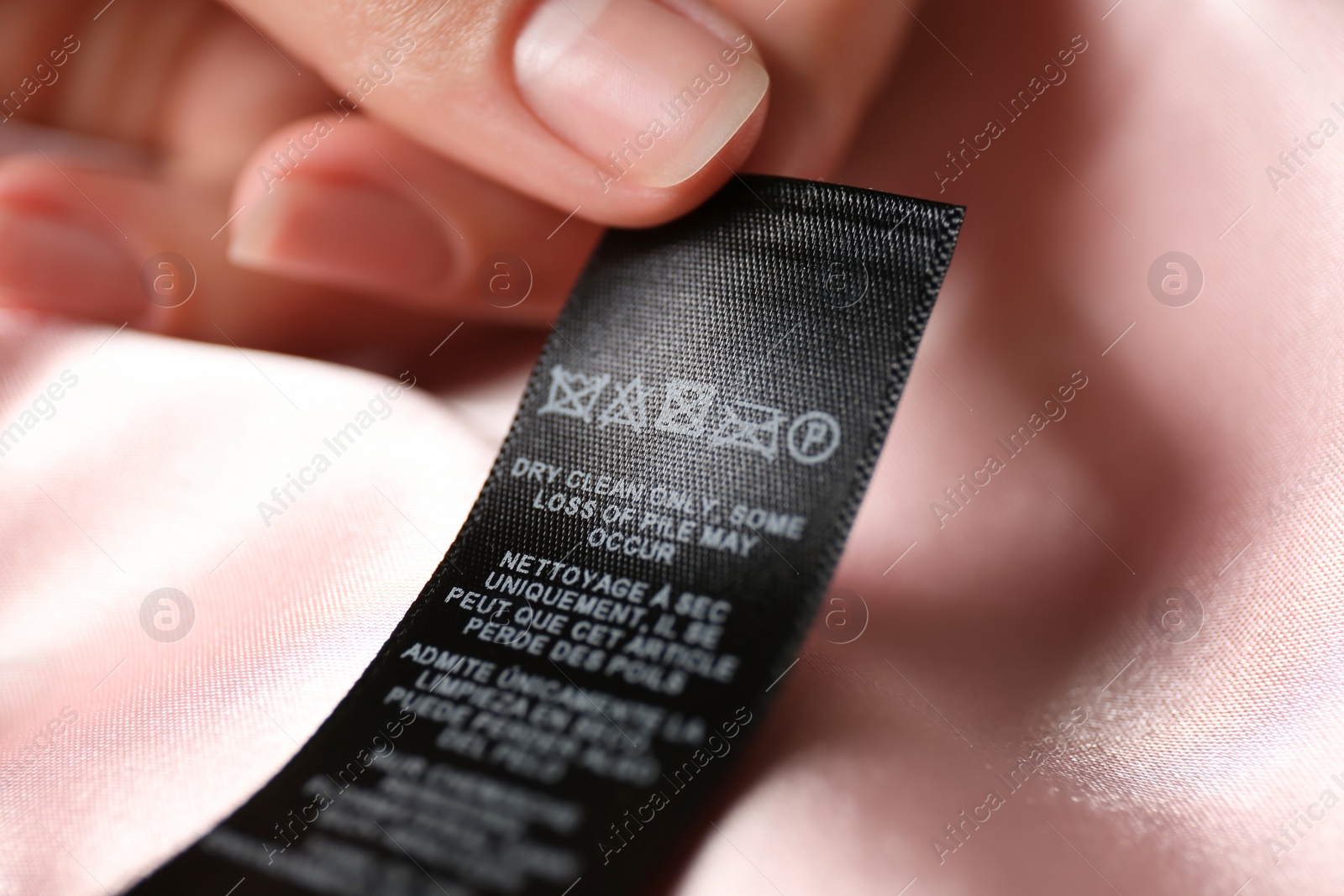 Photo of Woman reading clothing label with care symbols on pink silk shirt, closeup