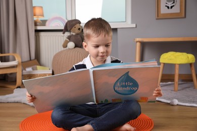 Cute little boy reading book on floor at home