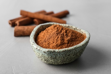 Bowl with aromatic cinnamon powder and sticks on grey background