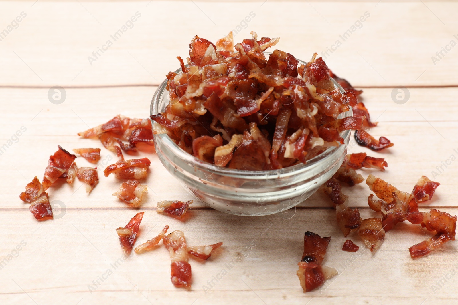 Photo of Pieces of tasty fried bacon in bowl on wooden table, closeup