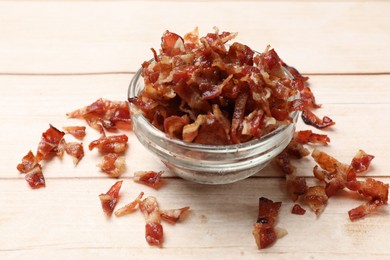 Photo of Pieces of tasty fried bacon in bowl on wooden table, closeup