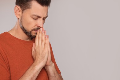 Man with clasped hands praying on light grey background. Space for text