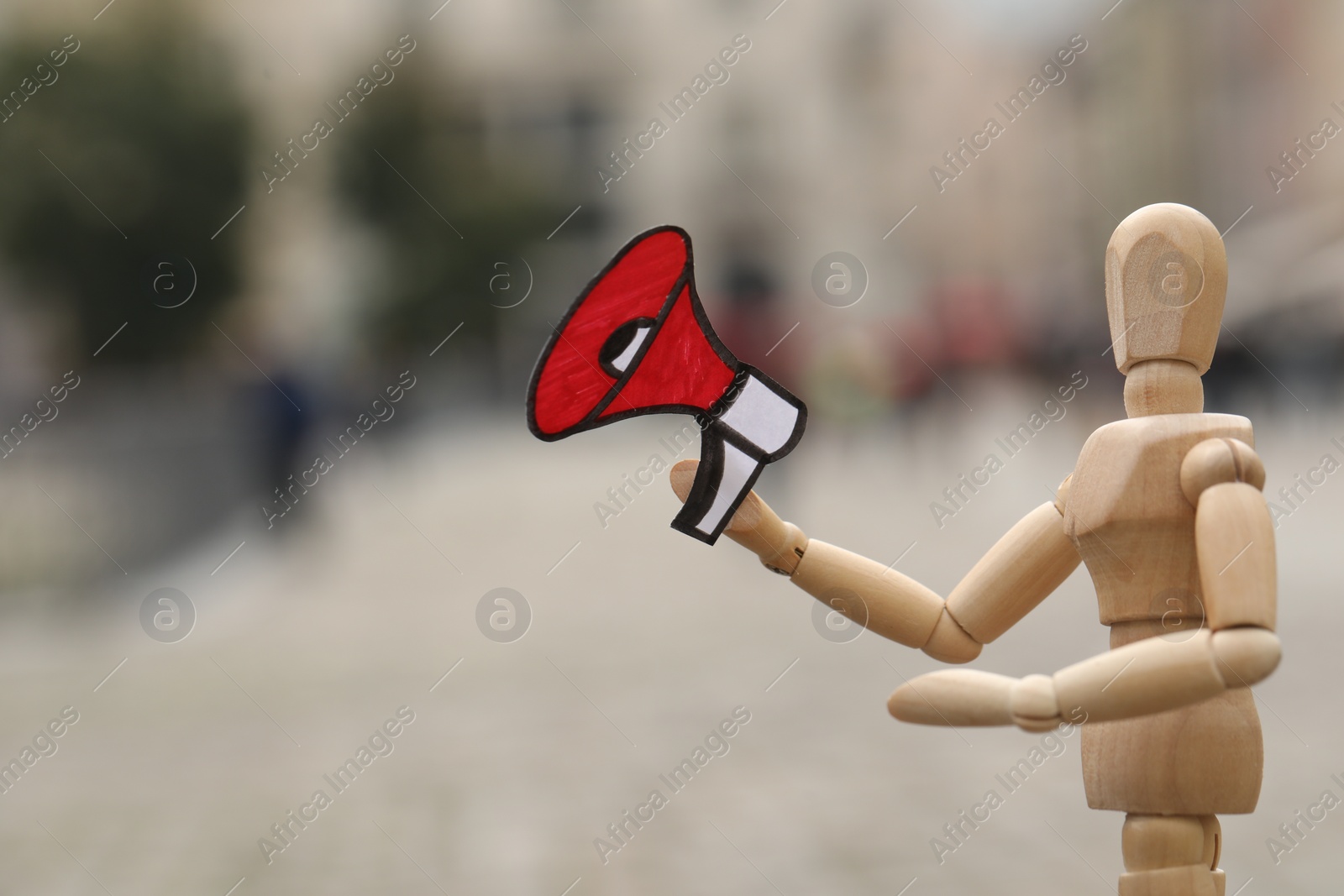 Photo of Wooden human figure with paper megaphone on city street, closeup. Space for text