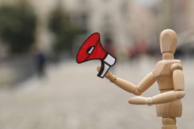 Wooden human figure with paper megaphone on city street, closeup. Space for text