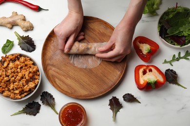 Photo of Woman making tasty spring roll at white marble table, top view