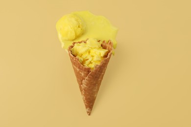 Photo of Melted ice cream in wafer cone on pale yellow background, top view