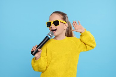 Photo of Cute little girl with microphone singing on light blue background