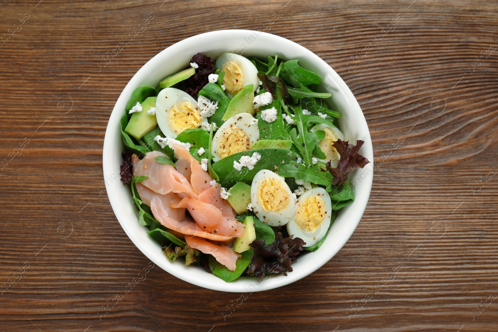 Photo of Delicious salad with boiled eggs, salmon and cheese in bowl on wooden table, top view