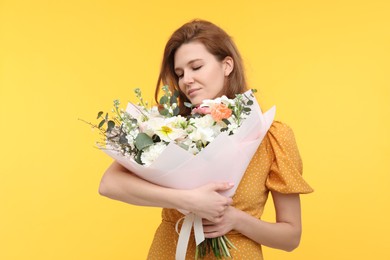 Beautiful woman with bouquet of flowers on yellow background
