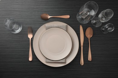 Photo of Stylish setting with cutlery, glasses and plates on black wooden table, flat lay