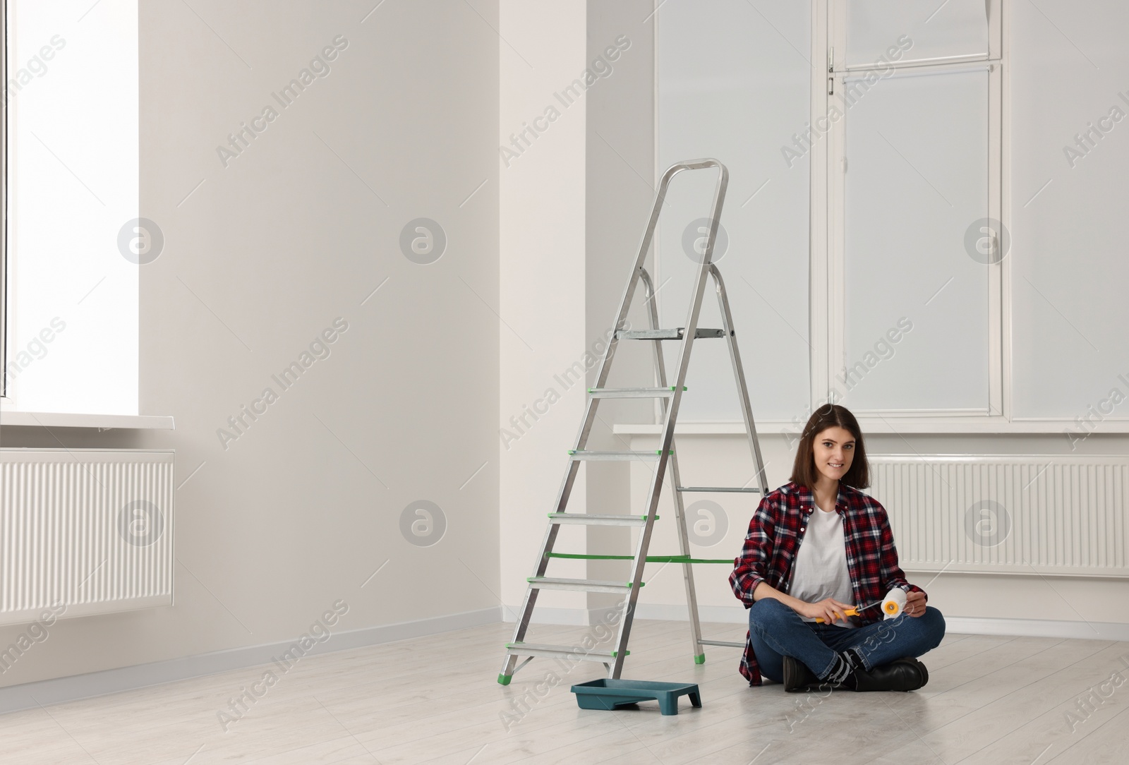 Photo of Young woman with roller sitting near stepladder indoors. Room renovation