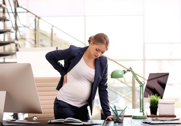 Photo of Young pregnant woman suffering from pain while working in office