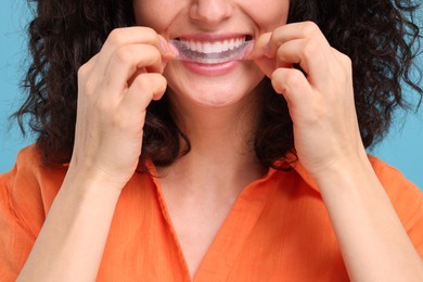 Photo of Young woman applying whitening strip on her teeth against light blue background, closeup