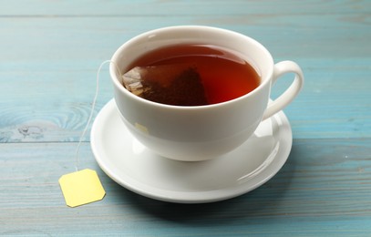 Photo of Tea bag in cup with hot drink on light blue wooden table, closeup