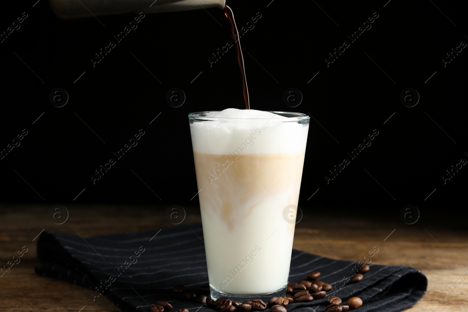 Photo of Making delicious latte macchiato on wooden table against black background