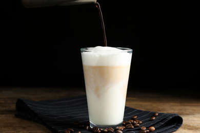 Making delicious latte macchiato on wooden table against black background