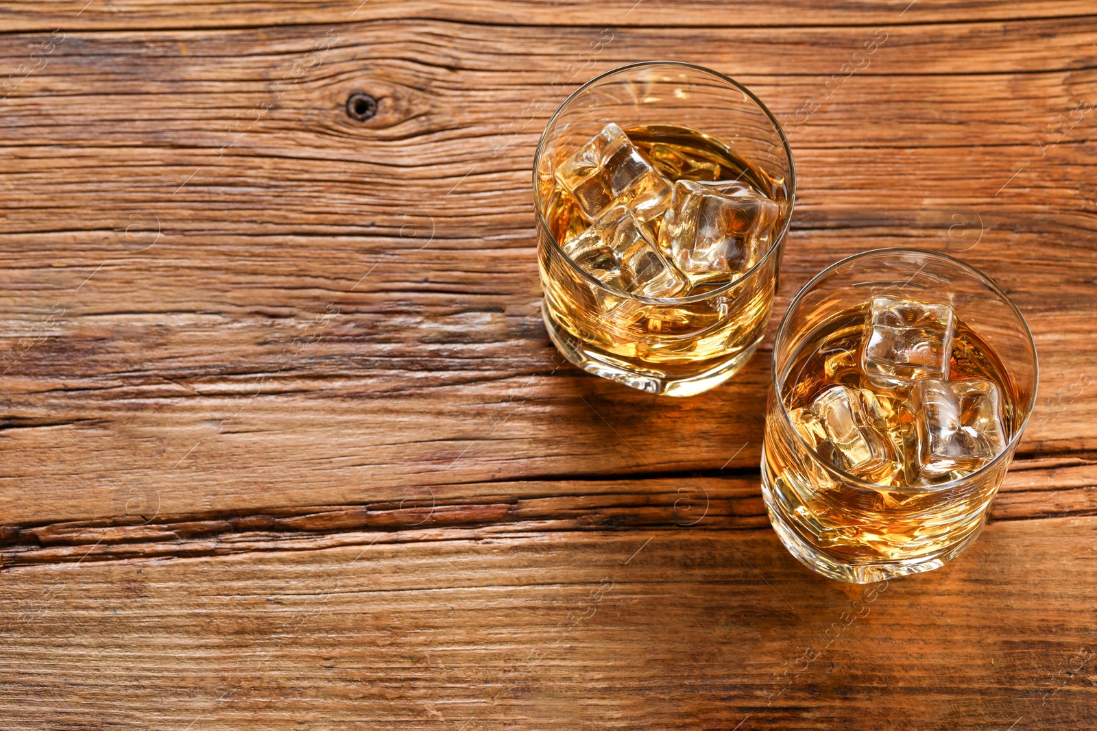 Photo of Whiskey with ice cubes in glasses on wooden table, above view. Space for text