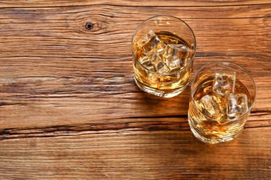Photo of Whiskey with ice cubes in glasses on wooden table, above view. Space for text