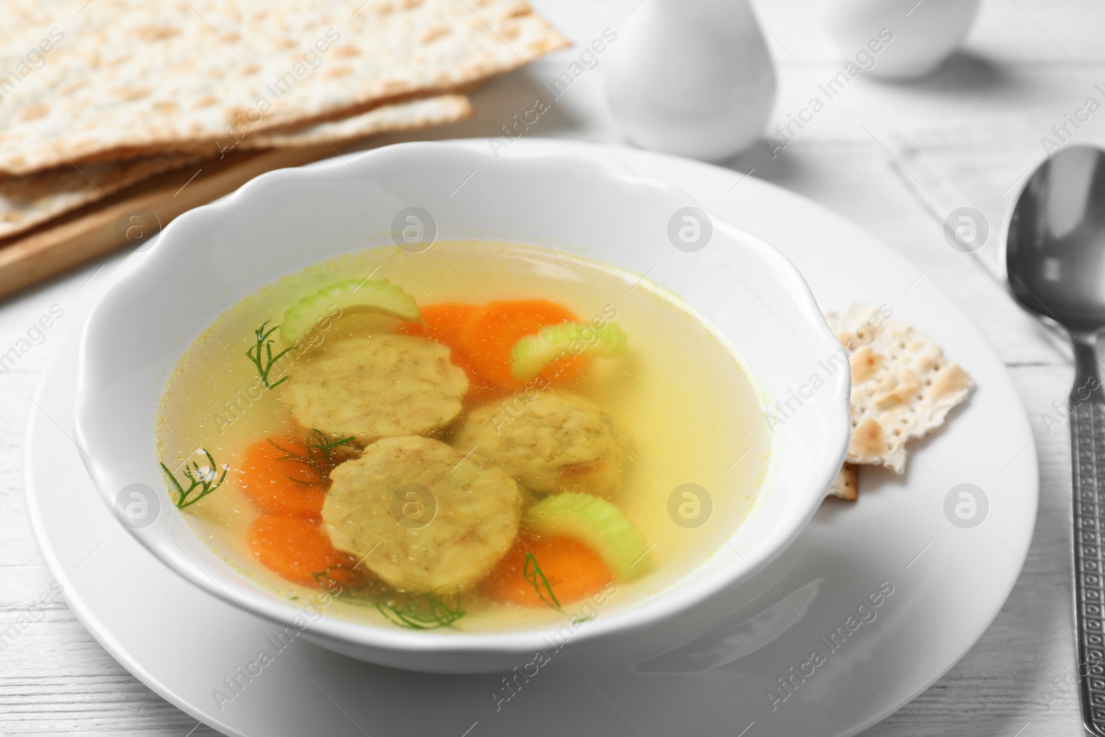 Photo of Bowl of Jewish matzoh balls soup on white wooden table