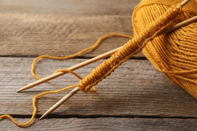 Photo of Soft orange yarn, knitting and needles on wooden table, closeup