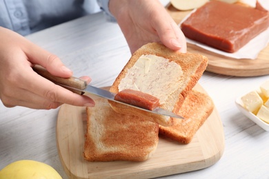 Photo of Woman spreading delicious quince paste on toast bread at white wooden table, closeup