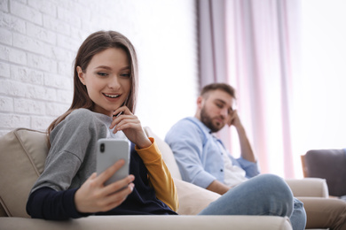 Young man peering into girlfriend's smartphone at home, focus on woman. Relationship problems