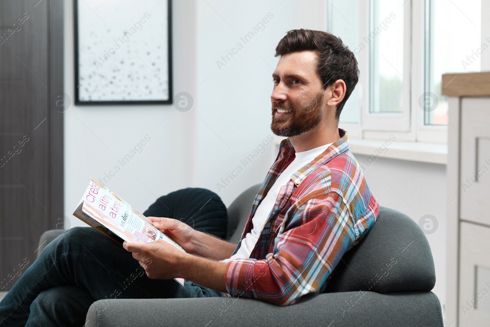 Photo of Smiling bearded man with magazine on sofa indoors