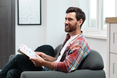 Smiling bearded man with magazine on sofa indoors
