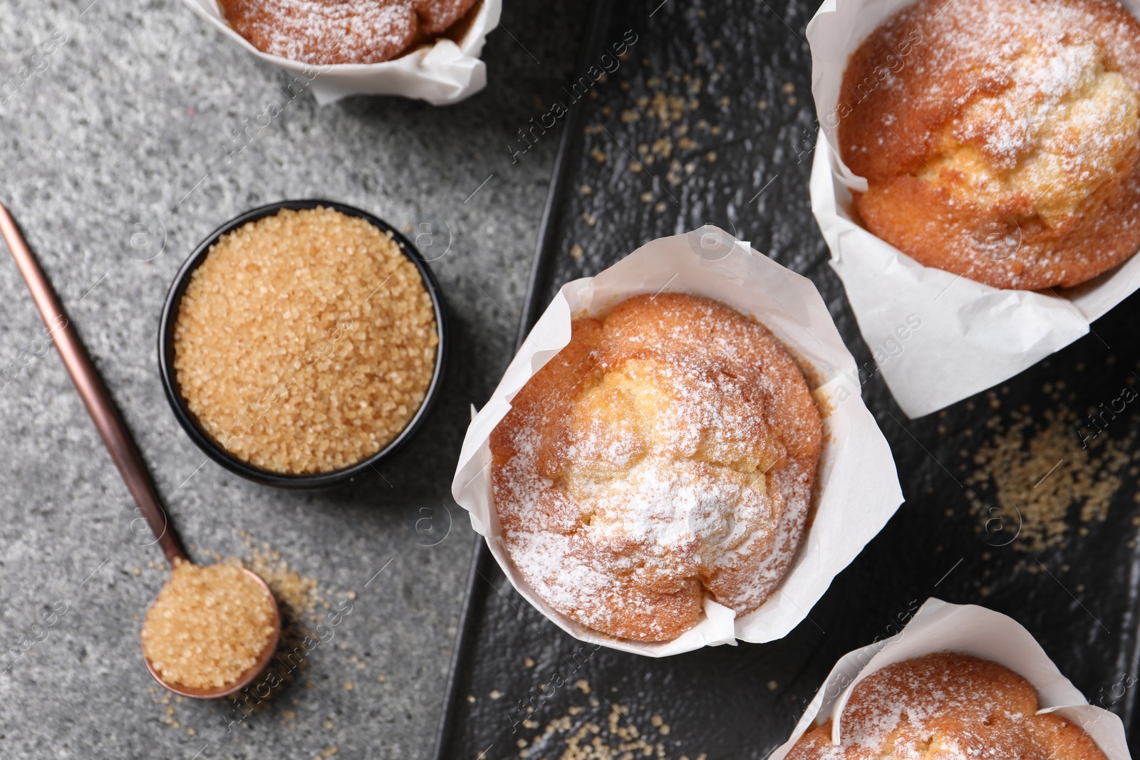 Photo of Delicious muffins and sugar on grey table, flat lay