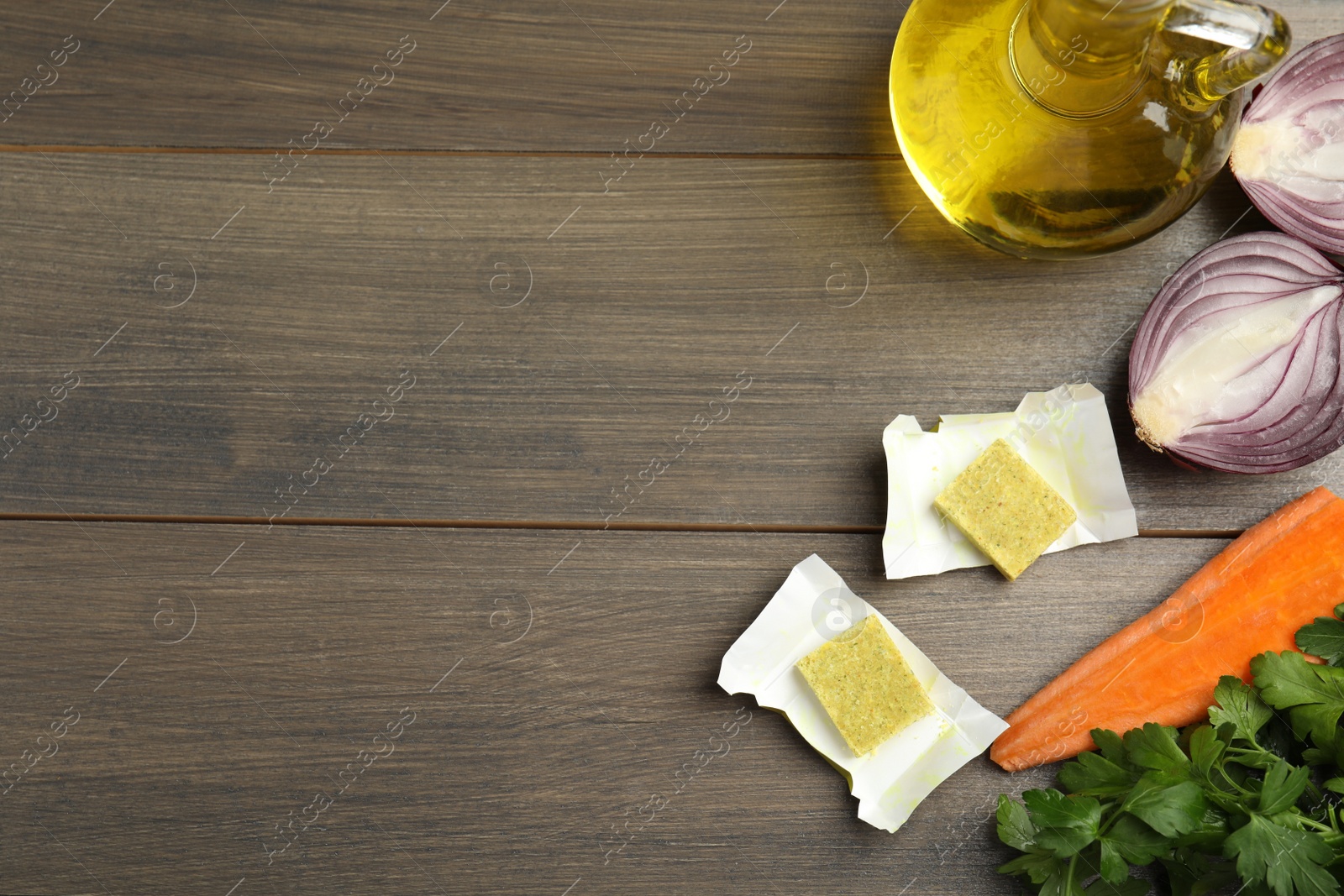 Photo of Bouillon cubes and other ingredients on wooden table, flat lay. Space for text