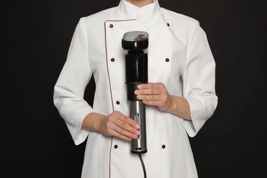 Chef holding sous vide cooker on black background, closeup