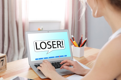 Young woman using laptop at wooden table, closeup. Cyber bullying