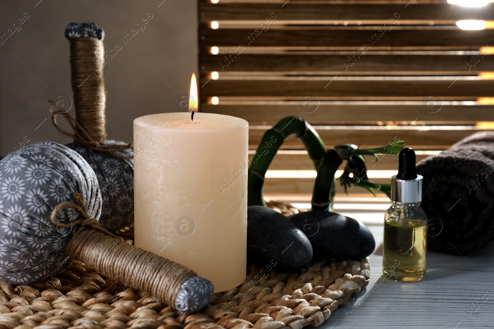Photo of Burning candle, herbal bags, spa stones and oil on wooden table