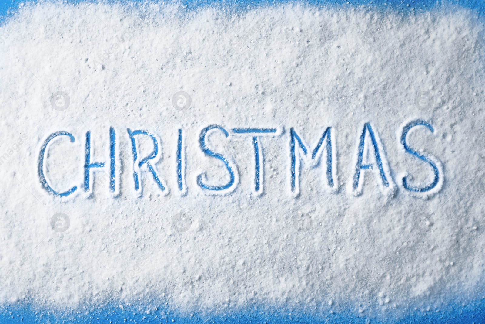 Photo of Word CHRISTMAS written in snow on color background, top view
