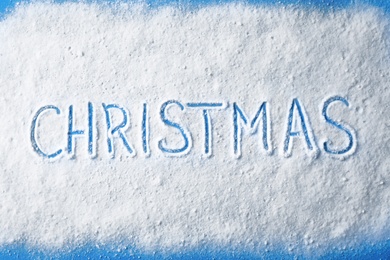 Word CHRISTMAS written in snow on color background, top view