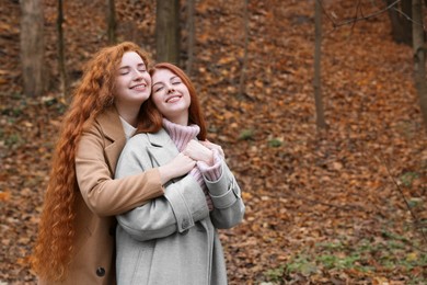 Photo of Portrait of beautiful young redhead sisters in park on autumn day. Space for text