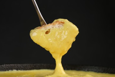 Photo of Dipping piece of bread into fondue pot with tasty melted cheese against dark gray background, closeup