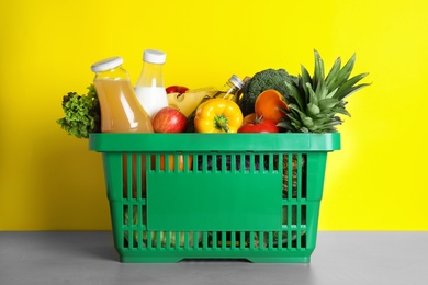 Photo of Shopping basket with grocery products on grey table against yellow background