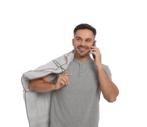 Man holding garment cover with clothes while talking on phone, isolated on white. Dry-cleaning service