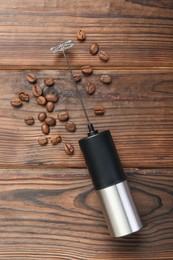 Photo of Black milk frother wand and coffee beans on wooden table, top view