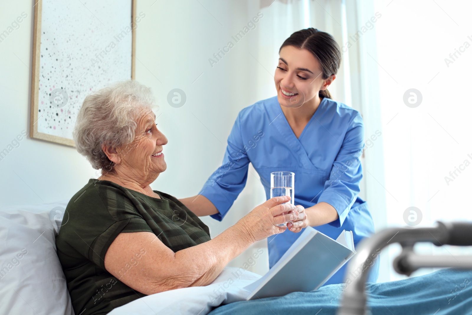 Photo of Care worker giving water to elderly woman in geriatric hospice