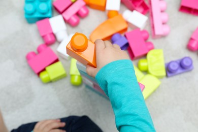 Top view of little child playing with building blocks on carpet, closeup