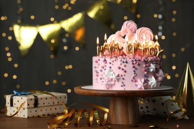 Photo of Beautiful birthday cake with burning candles and decor on wooden table. Space for text