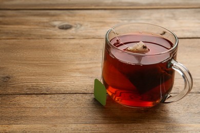 Photo of Tea bag in glass cup of hot water on wooden table. Space for text